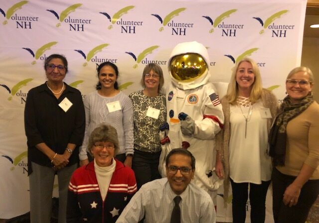 Group of professionals posing with a person in an astronaut suit at an event.