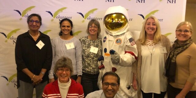 Group of professionals posing with a person in an astronaut suit at an event.