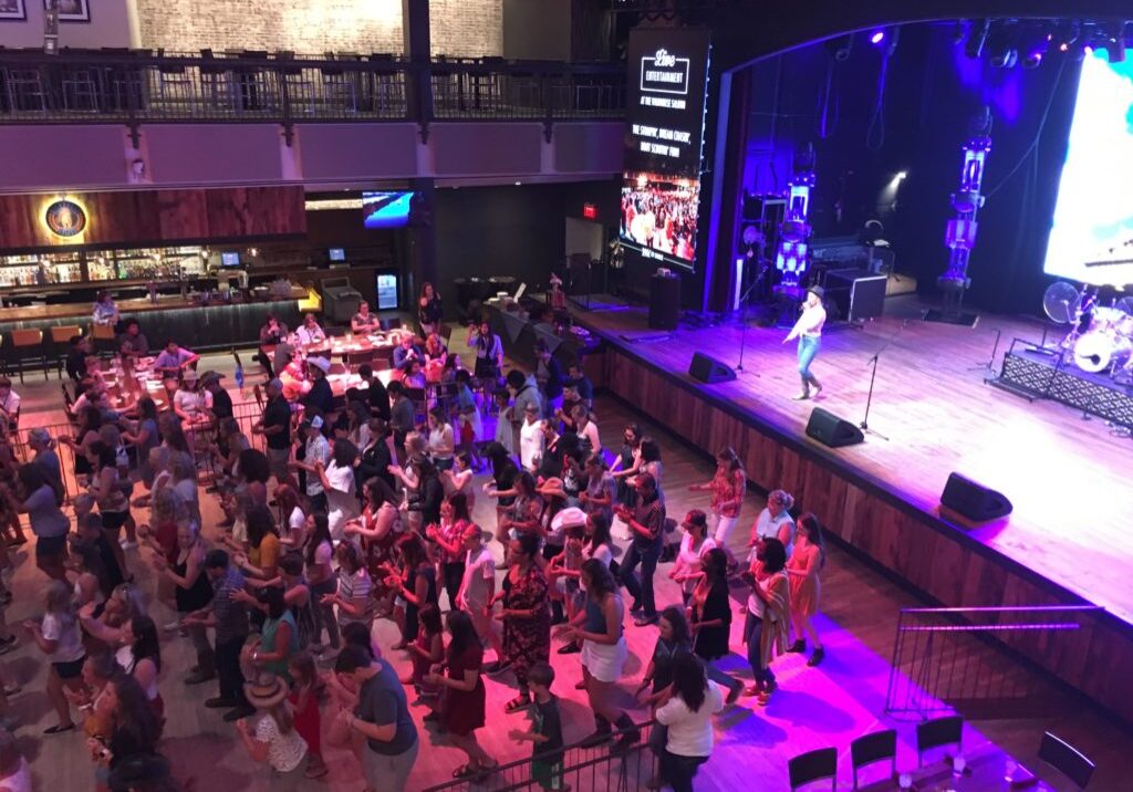 Crowd watching a live performance on stage in a large indoor venue.