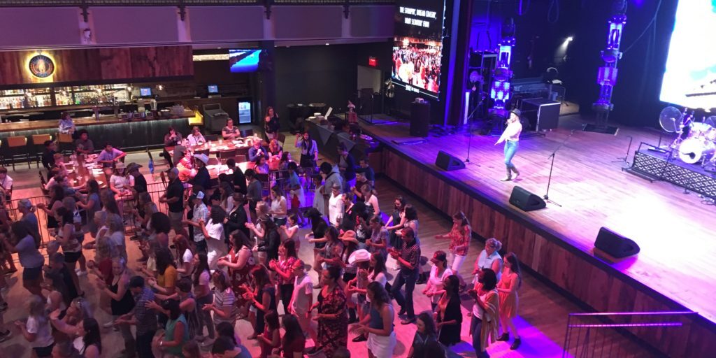 Crowd watching a live performance on stage in a large indoor venue.