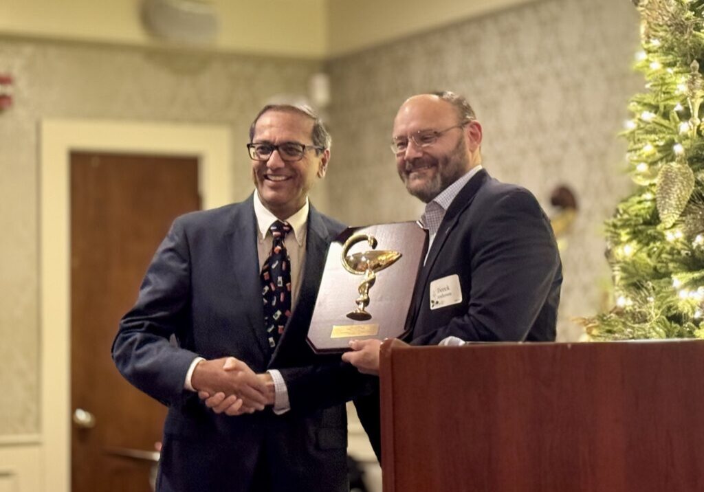Two men shaking hands during an award presentation at a formal event.