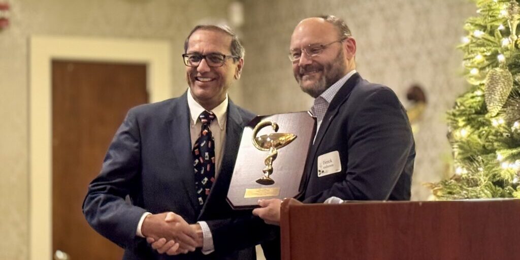 Two men shaking hands during an award presentation at a formal event.