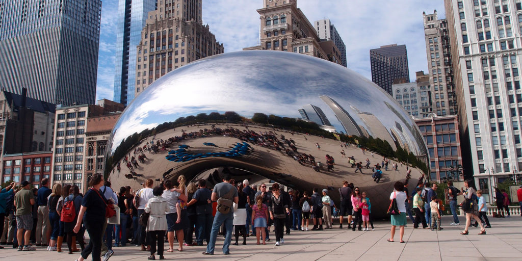 The Cloud Gate sculpture in Chicago filled with visitors on a sunny day.