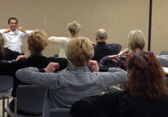 A group of people seated, raising their arms in unison during a session.