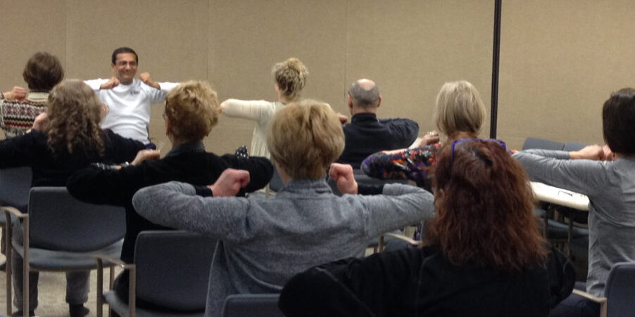 A group of people seated, raising their arms in unison during a session.
